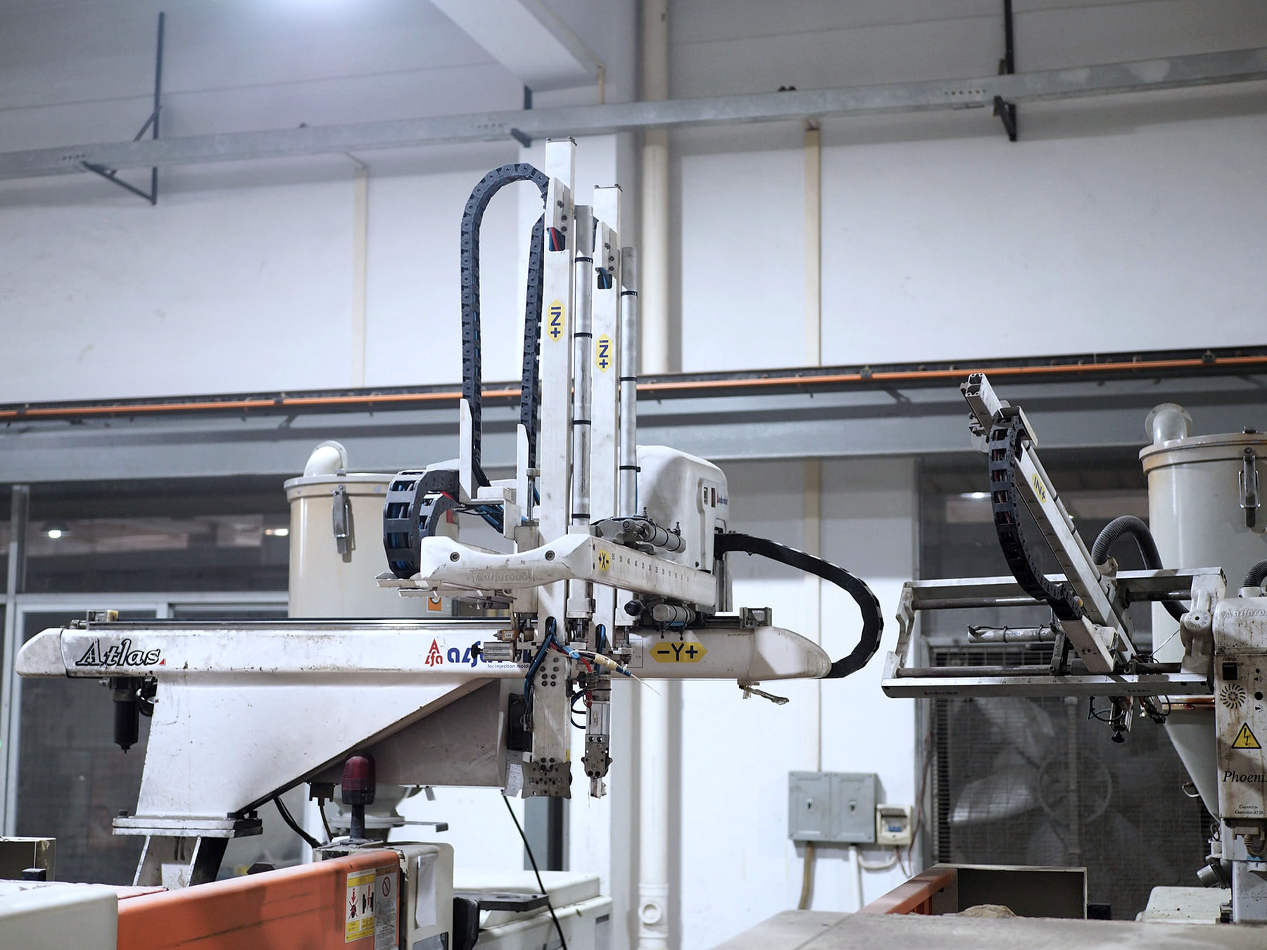 Automated part-handling equipment beside injection molding machinery.