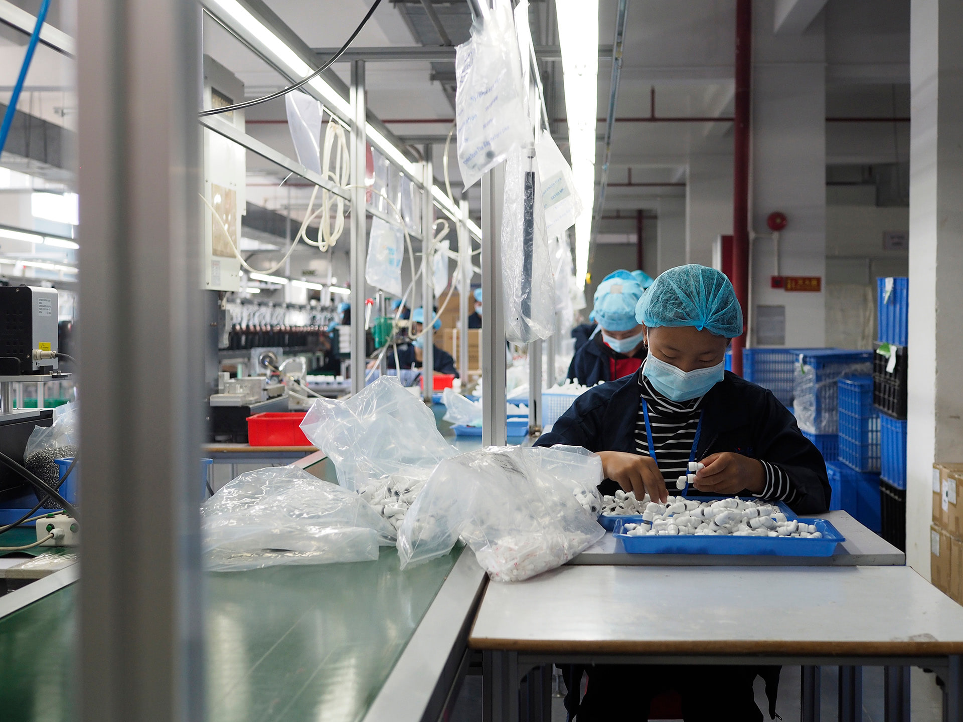 Masked production worker handling components at a dedicated workstation.