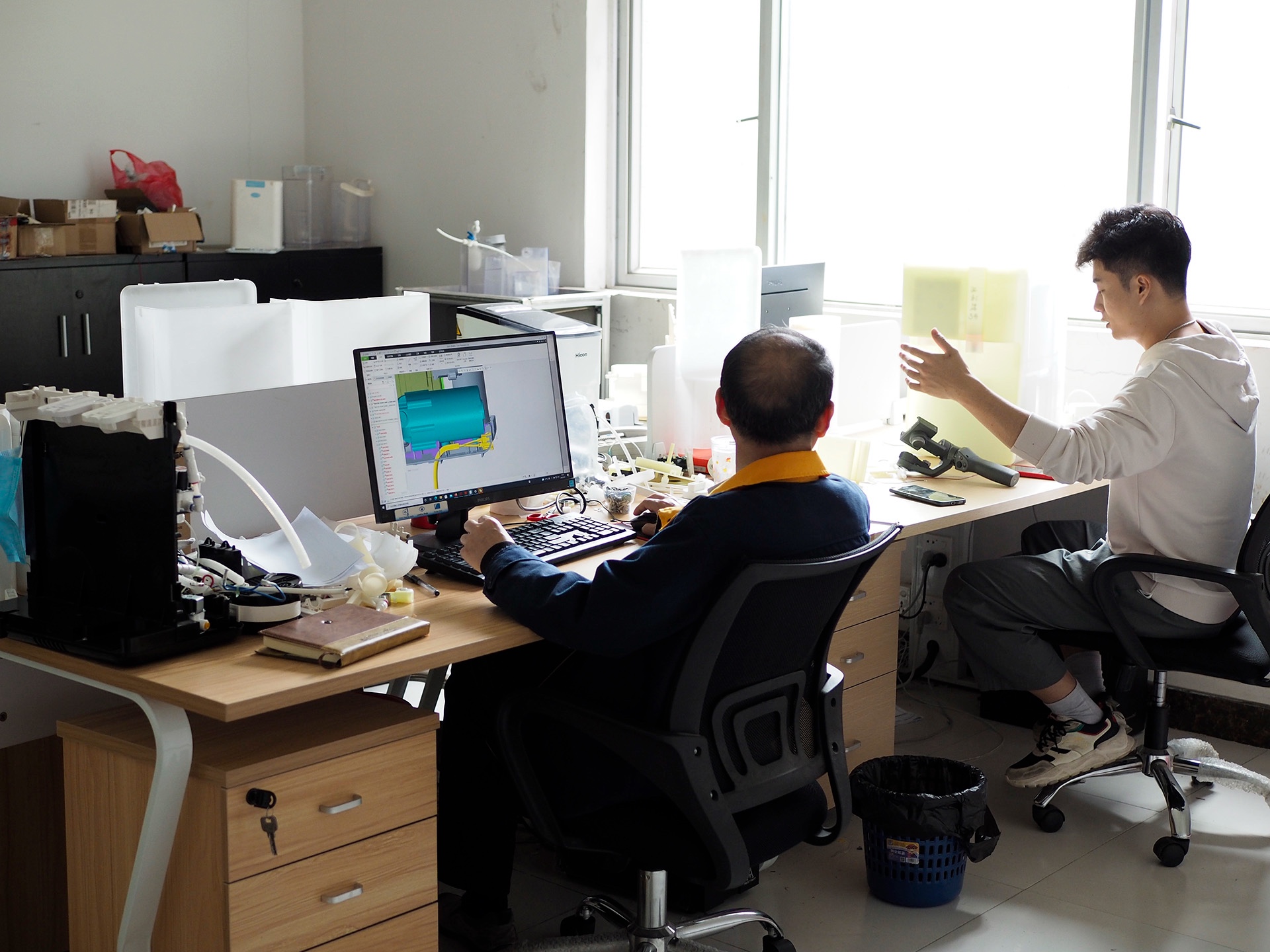 Engineers reviewing a water-system CAD model and physical prototypes.